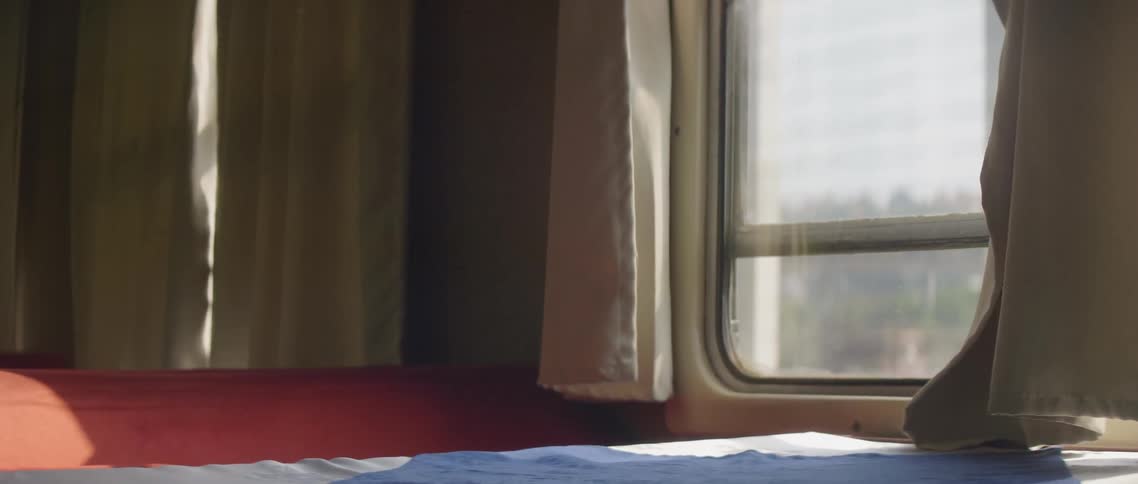 White curtain hangs by the train window as it travels on a sunny day