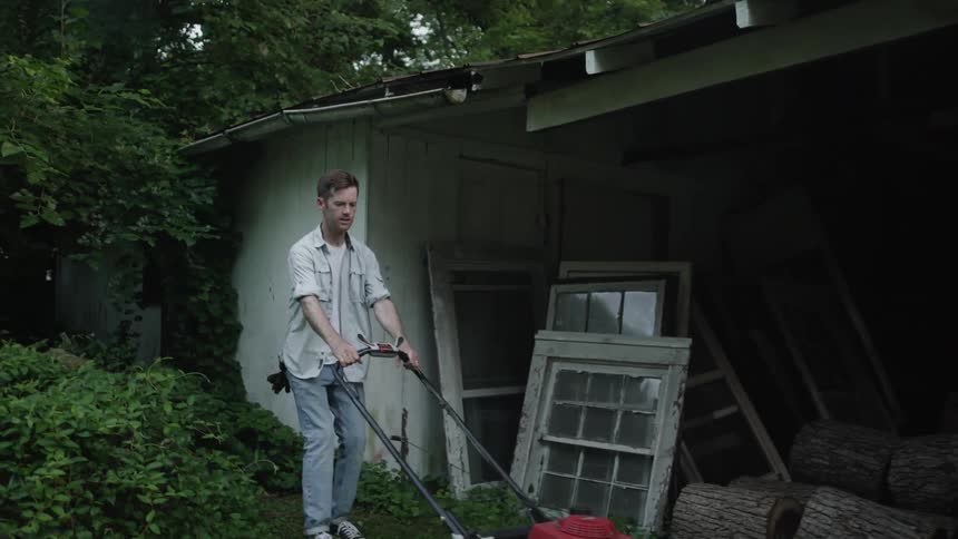 The man pushes the lawnmower around the yard