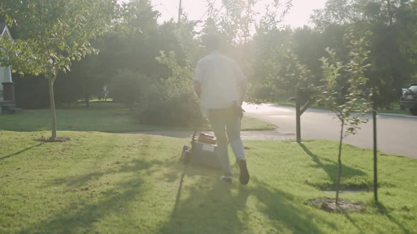 Man pushes a lawn mower across the grass on a bright sunny day