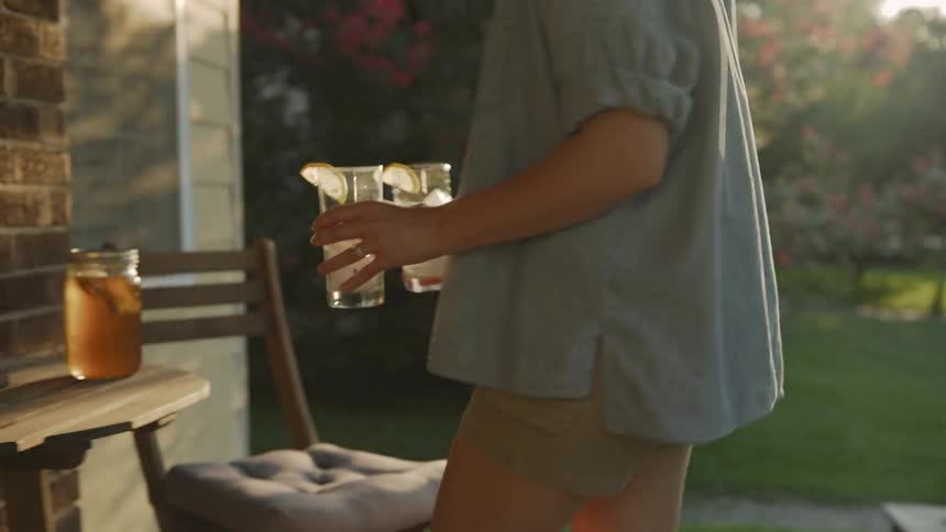 A man carries drinks on a sunny front porch