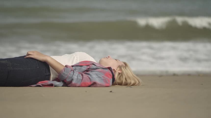 Woman with blond hair lays on the beach as waves roll in