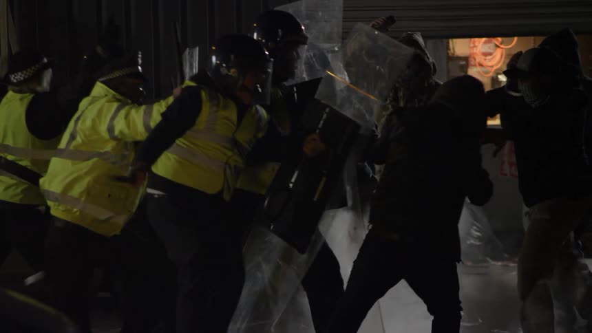 Guards holding shields try to fight off an angry mob