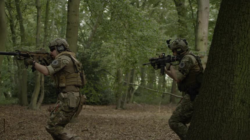 Military members walk through a forest with their guns drawn