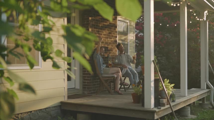 The two people talk and drink on the porch