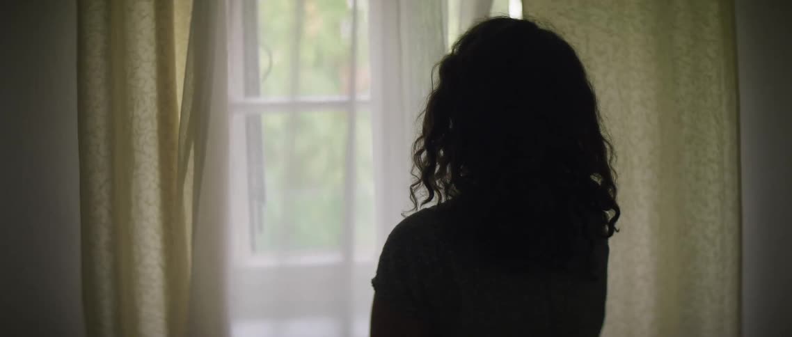 A woman pulls back a curtain to look out a window