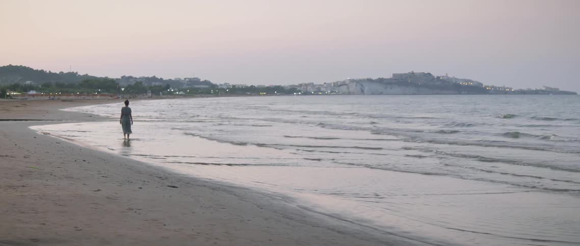 The woman is walking in the surf at sunset
