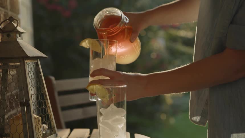 Hands Pour Sun Tea Into Glasses of Ice
