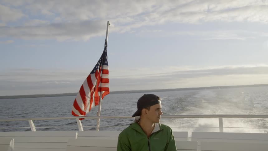 Man rides on a boat in a lake as a flag waves behind him