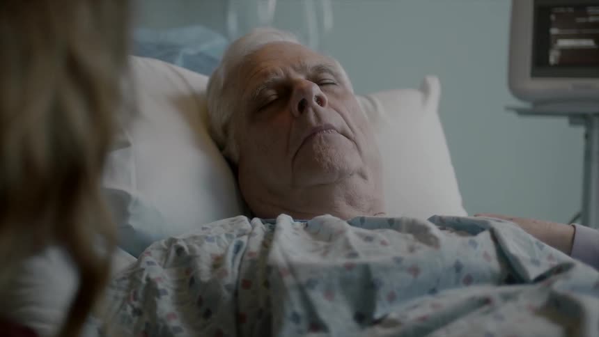 Elderly male patient sleeping as young woman sits bedside at the hospital