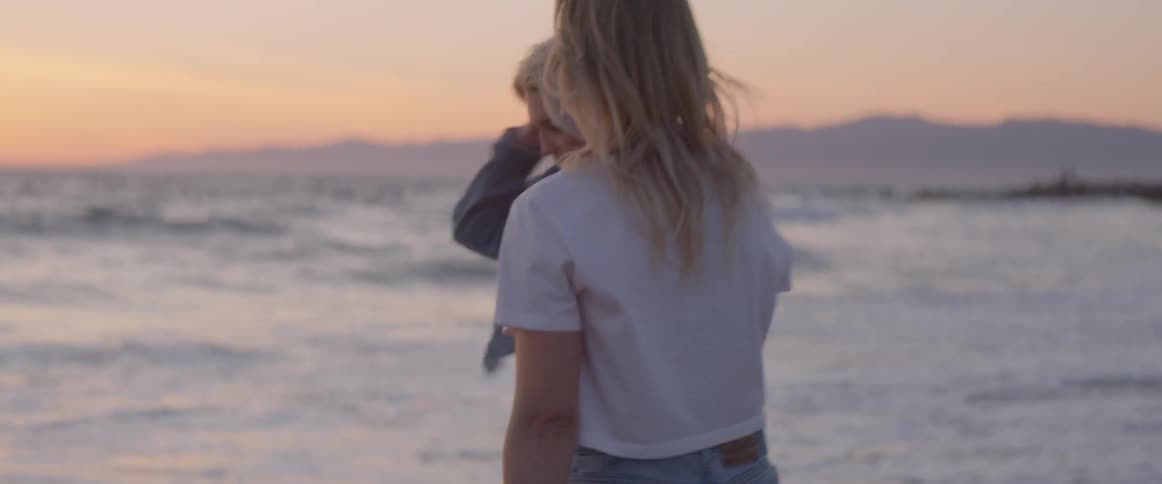 Two blond women hugging on the beach at sunset start to walk