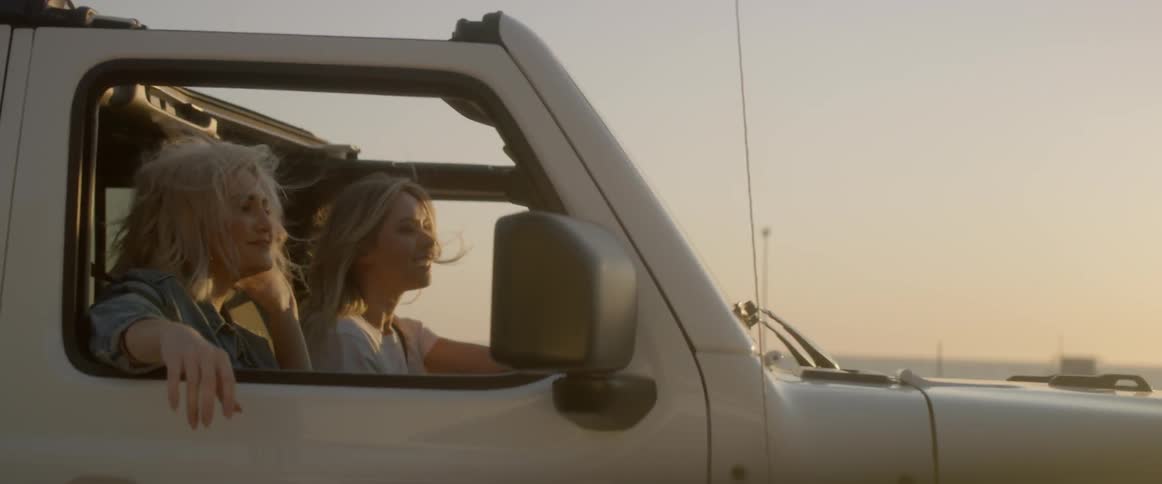 Two women ride in a vehicle with the windows down at sunset
