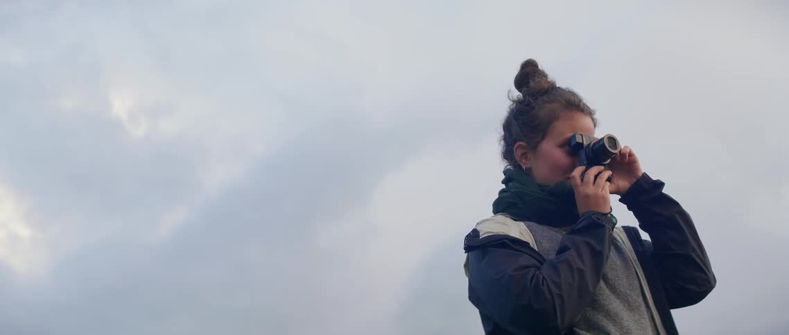 A woman takes a photograph outside on a cloudy day