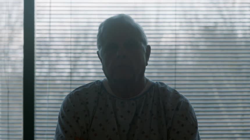 An older man sitting in front of a window on a cloudy day