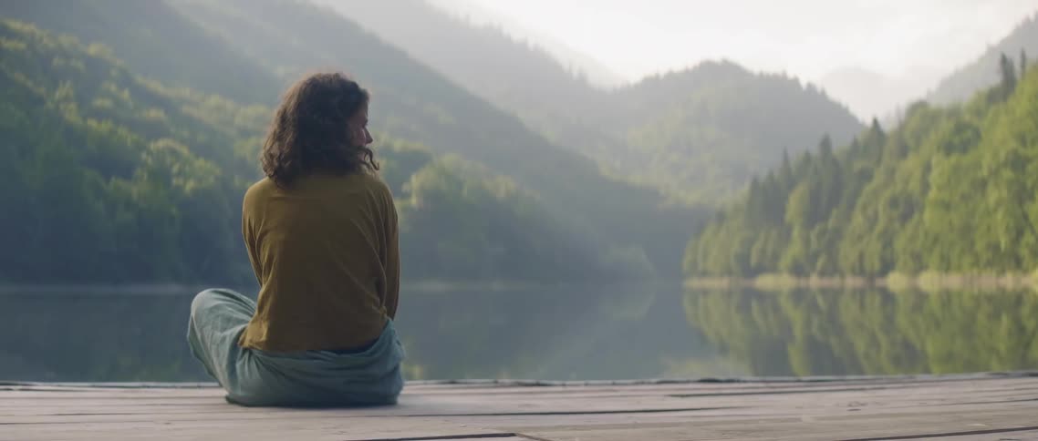 The woman sits on the pier by the lake