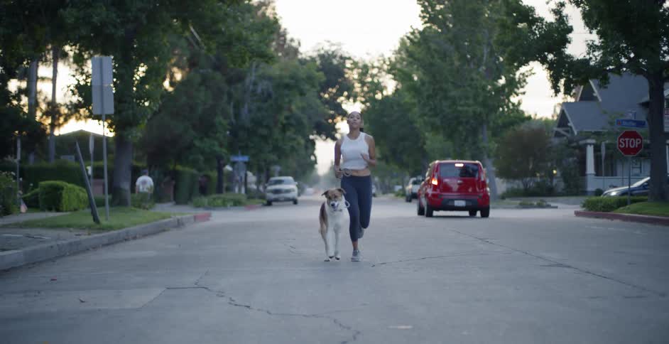 The woman runs down the street past the red car with her dog