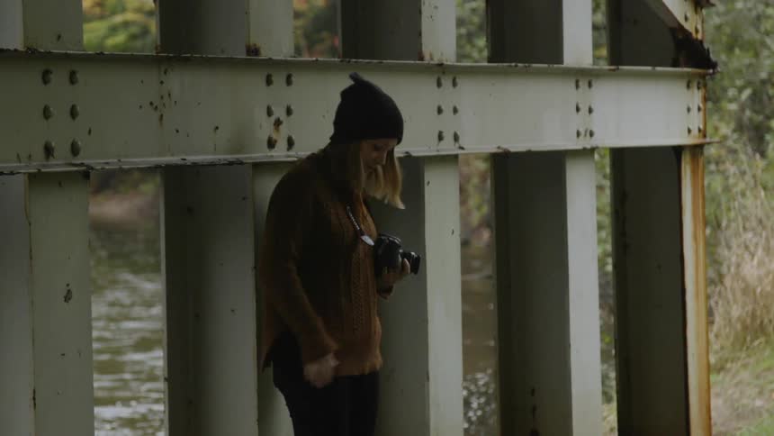 A woman takes a photograph beneath a river bridge