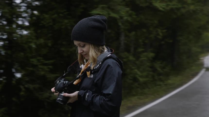 Woman looks down at her camera while walking on a narrow country road