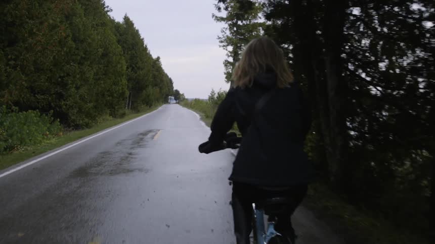 The woman is riding her bicycle on the wet road