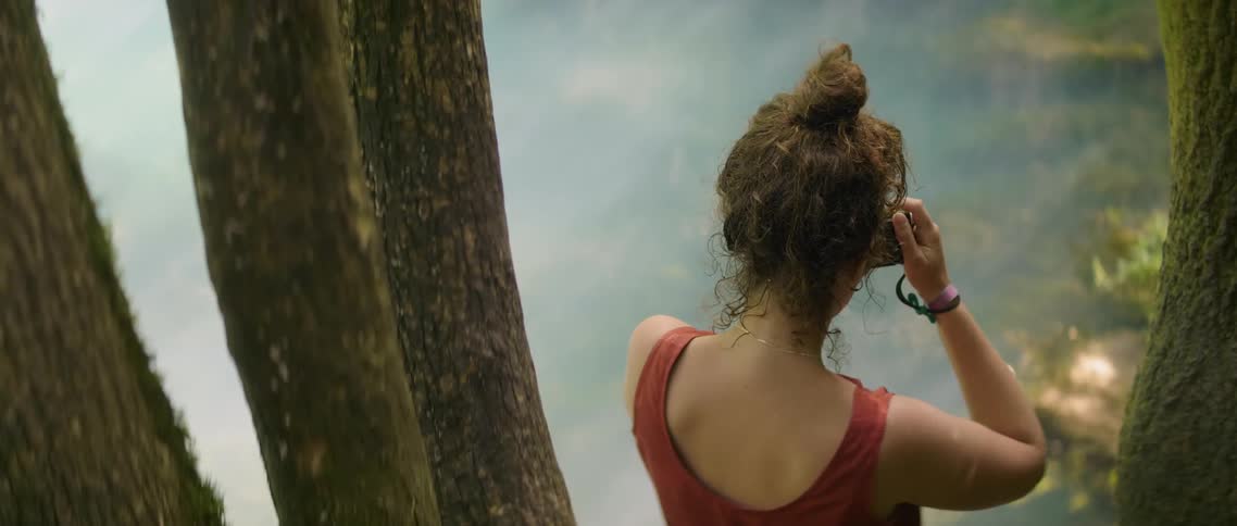 A woman stands near trees and takes photographs