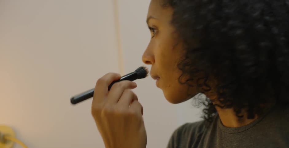 The woman is using the brush to put makeup on her cheeks