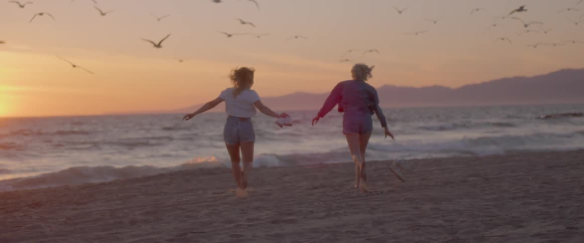 Two women run on a sandy beach at sunset