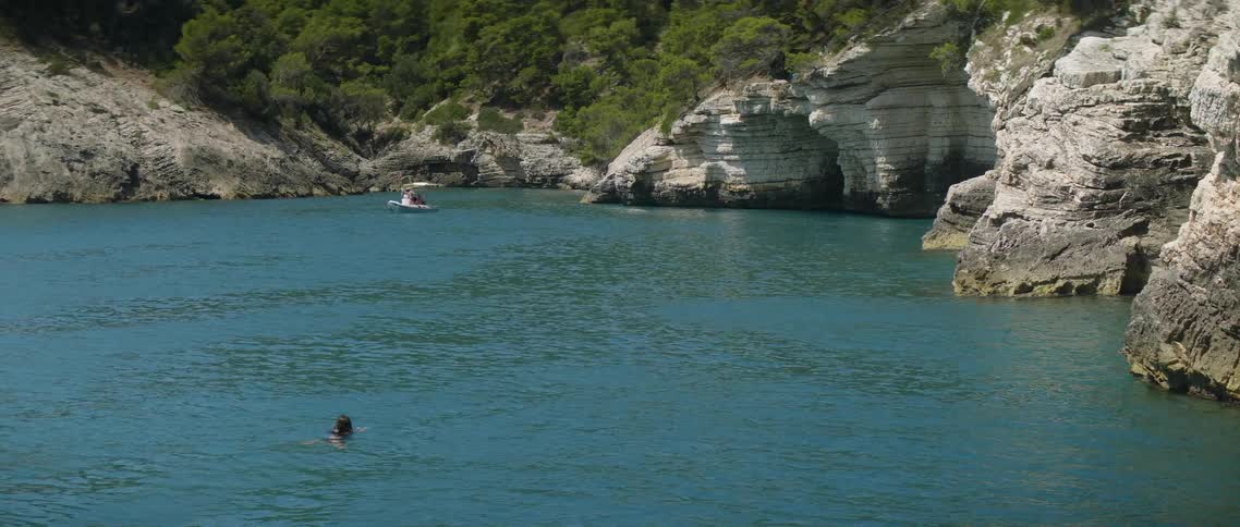 Woman swims in a lagoon as a boat floats nearby