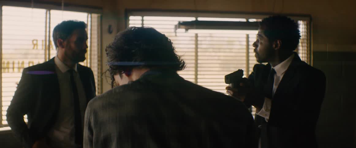 A man with a partner holds a gun aimed at a younger man in a store