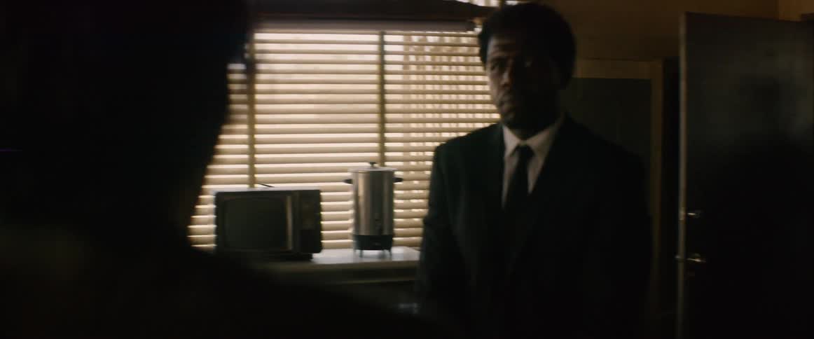 The man enters the room with a gun and points it at someone