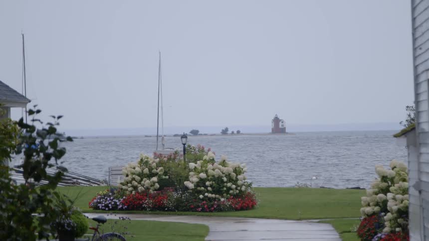 Sailboat masts sway in the wind near a home on shore