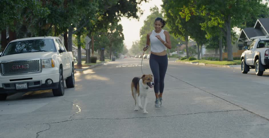 Woman holds a dog on its leash as they both jog down the street