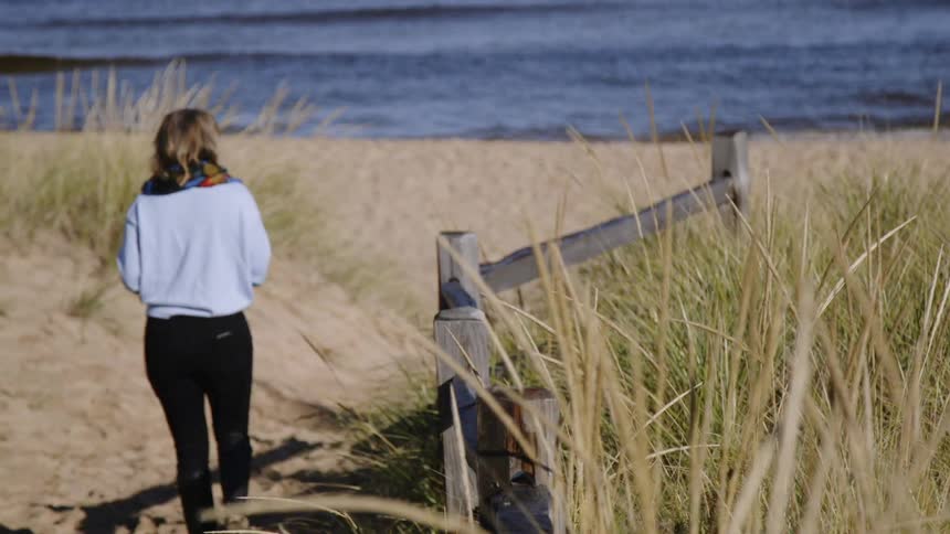 The woman walks towards the water on a windy day