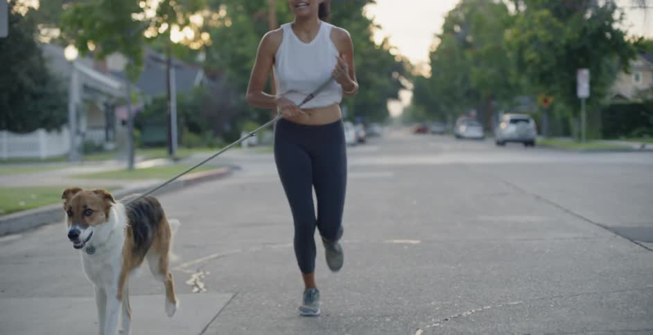 Woman jogs down the street with her dog on a leash