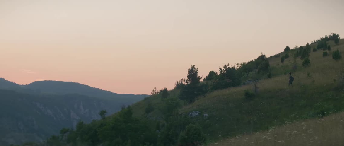 A hiker walks on a mountainside at sunset