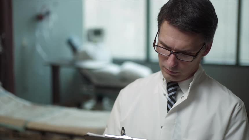 Man in a lab coat writing on a clipboard