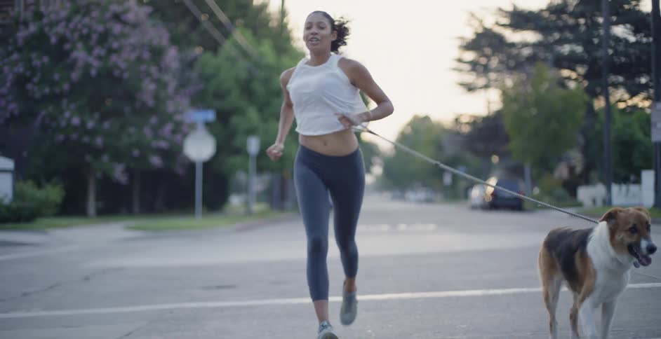 Woman in a ponytail jogs down the street with a dog on a leash