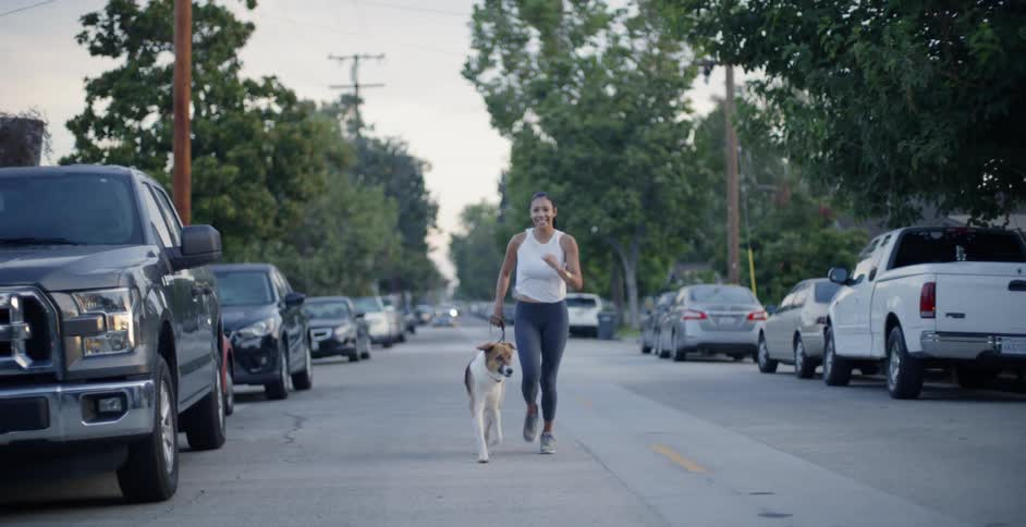 A woman and dog jog on a neighborhood street