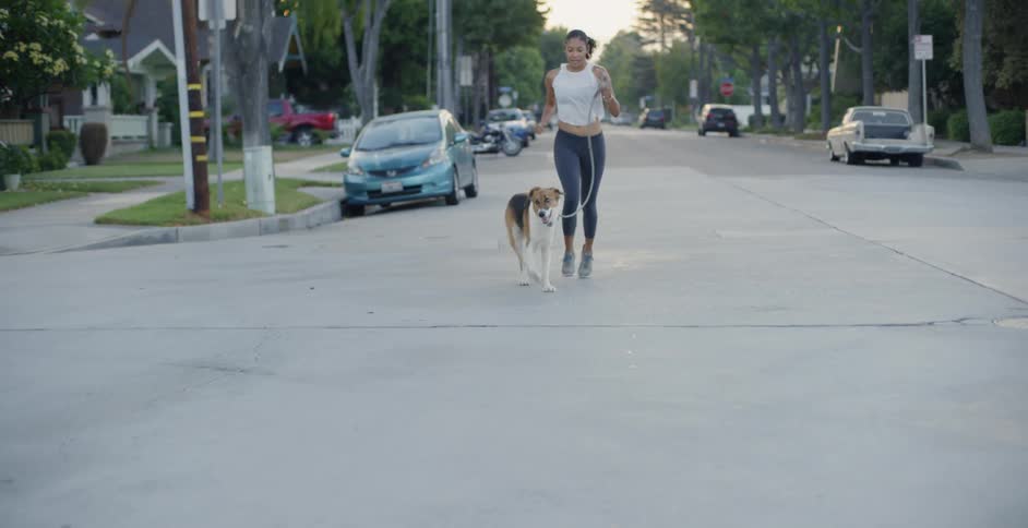 A woman and dog jog in a neighborhood at sunset