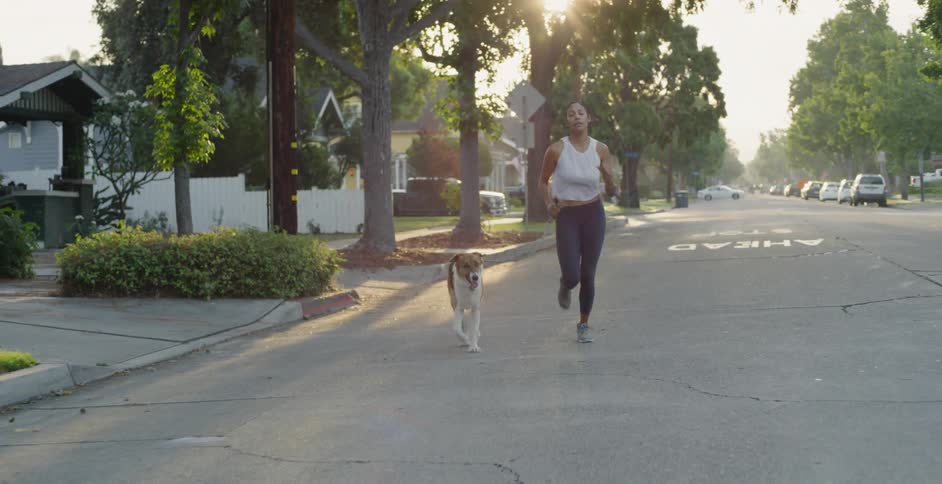 A woman and dog jog on a neighborhood street