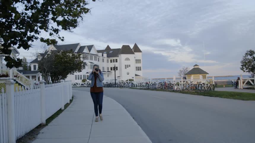 A woman takes a photograph of bicyclists in a town