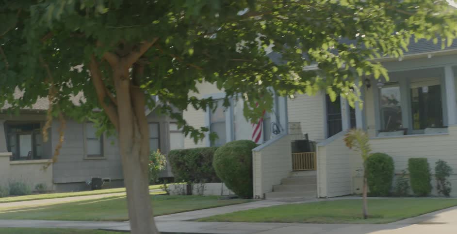 An american flag hangs on a pole on the front porch of a house in a neighborhood