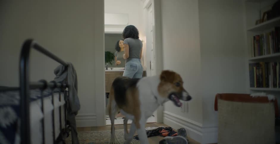 Woman primps in front of a mirror as a dog walks away from her