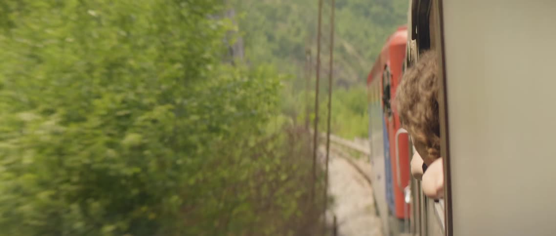 A person leans out the open window of a moving train