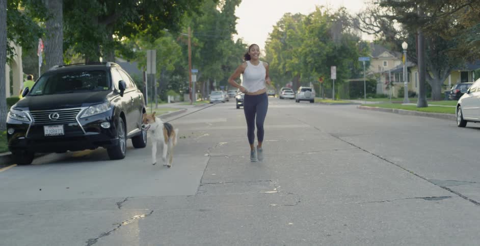 A woman and dog jog on a neighborhood street