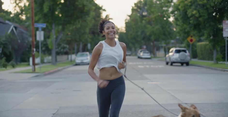 The woman is smiling as she jogs with her dog