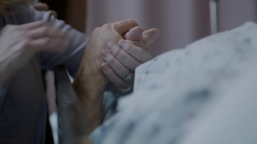 People comforting a person lying in a hospital bed