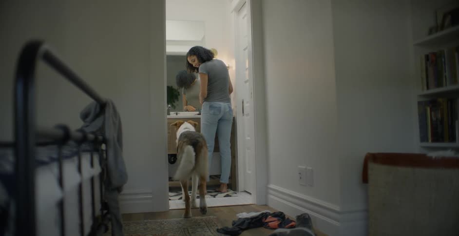 The woman pets her dog in the bathroom ahead