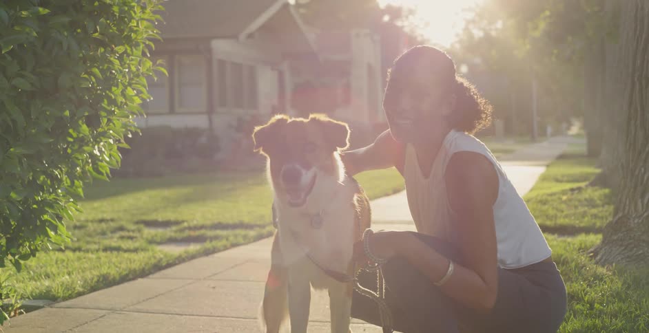 The woman pets her dog on the sidewalk of the neighborhood