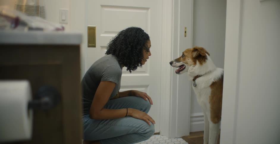 A woman pets and talks to a dog in a bathroom