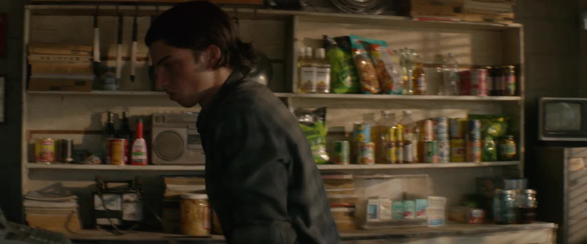 Man sits behind the counter of a small shop and gets up to walk around