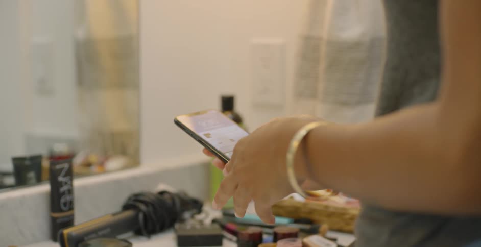 Woman picks up her cellphone as she stands at the bathroom sink